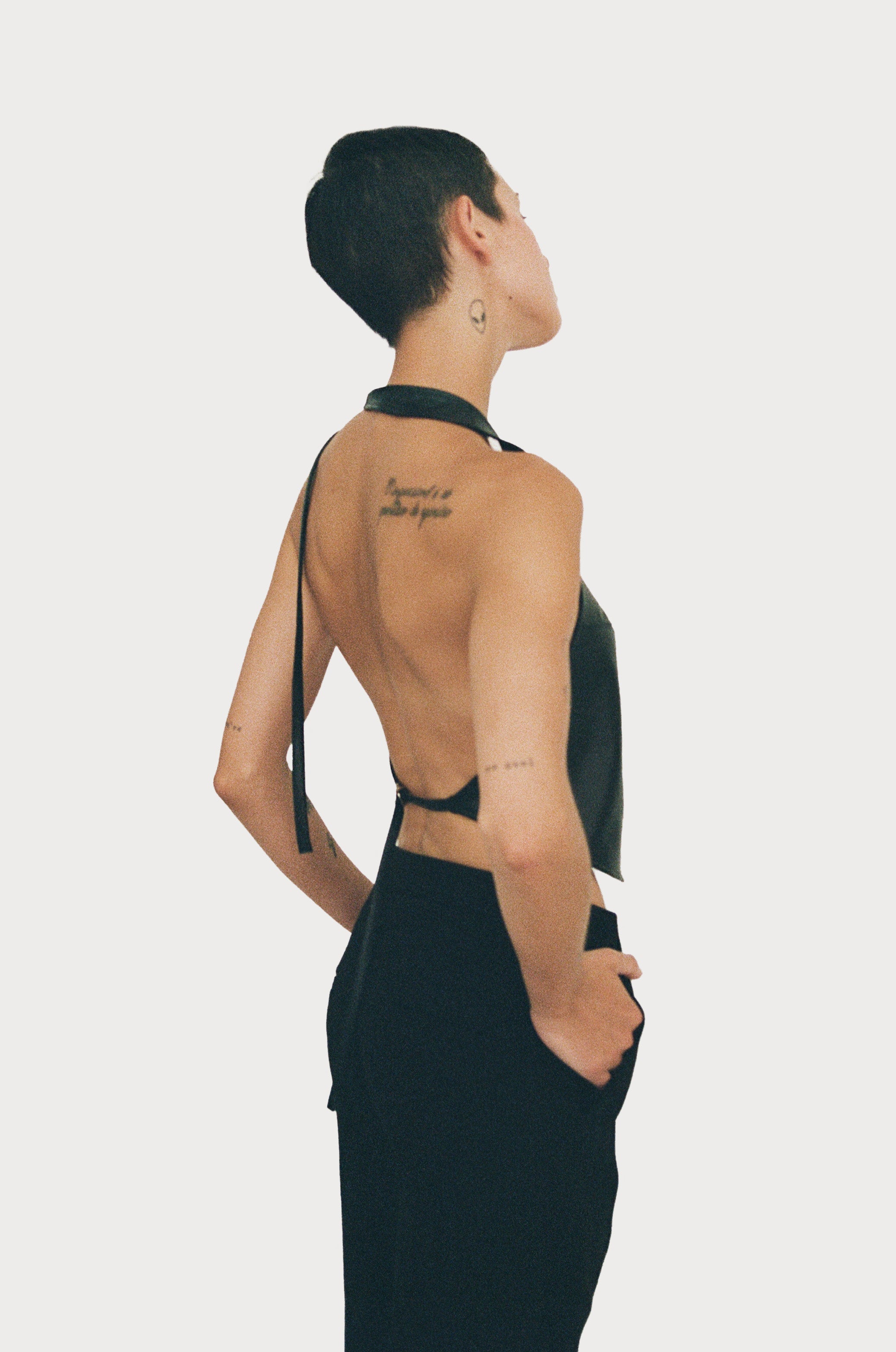 a female model wearing black yvy leather halter neck top with open back and black pants, side view