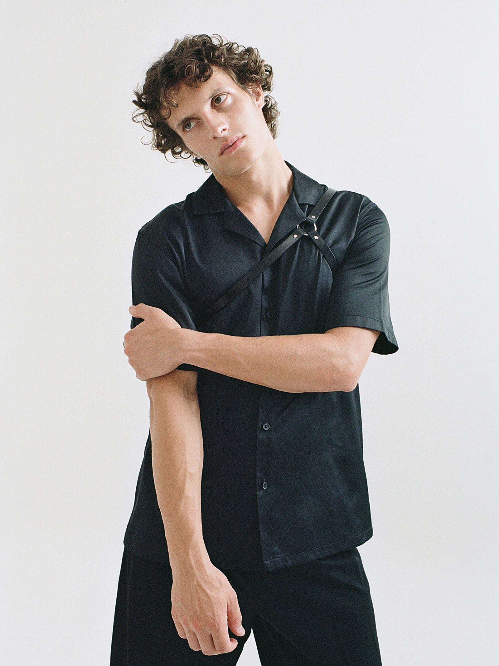 A male model wears the leather asymmetric shoulder piece with a black collared shirt and black pants