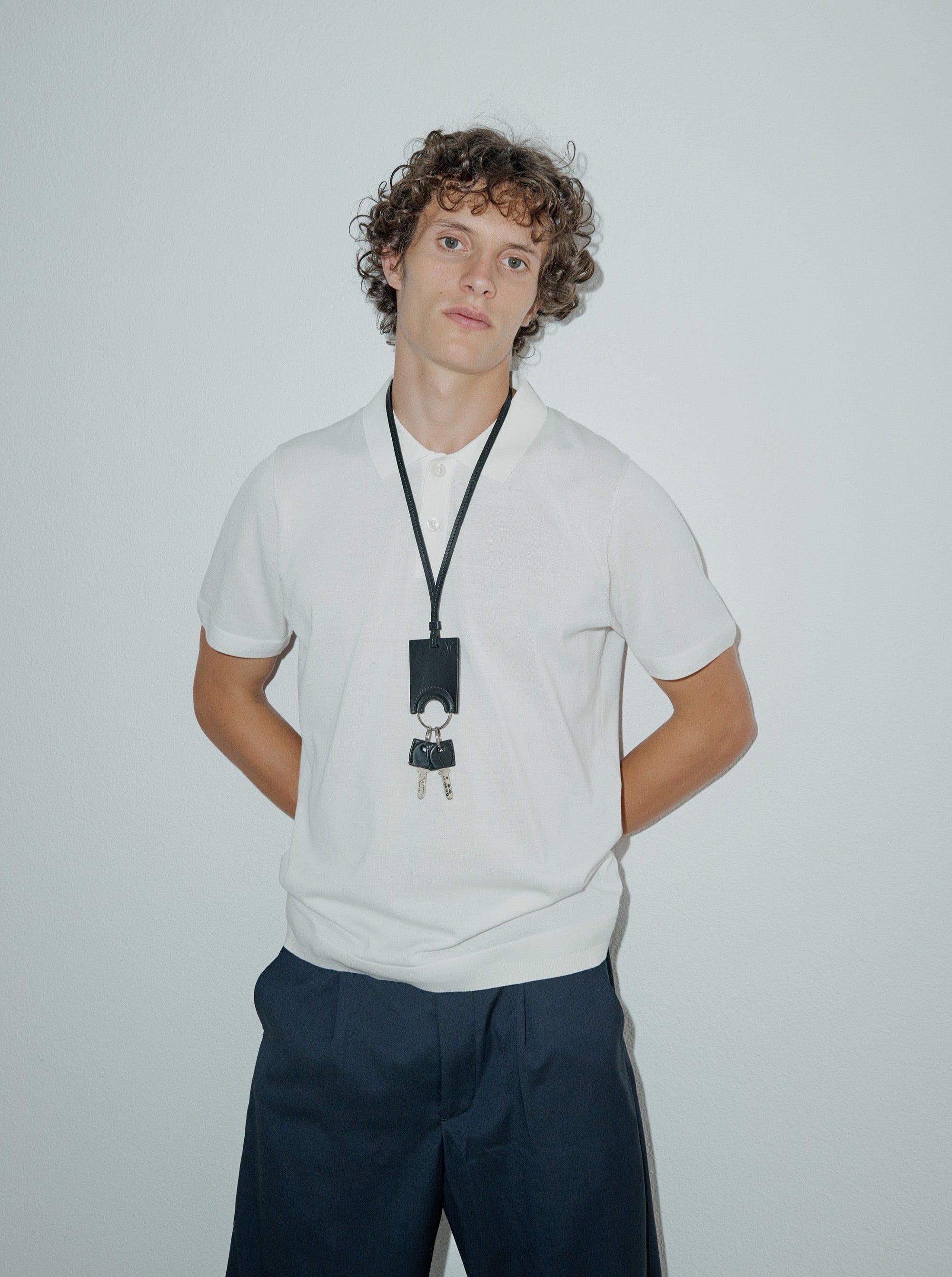 man wearing yvy long leather ring key holder with key covers over white polo t-shirt