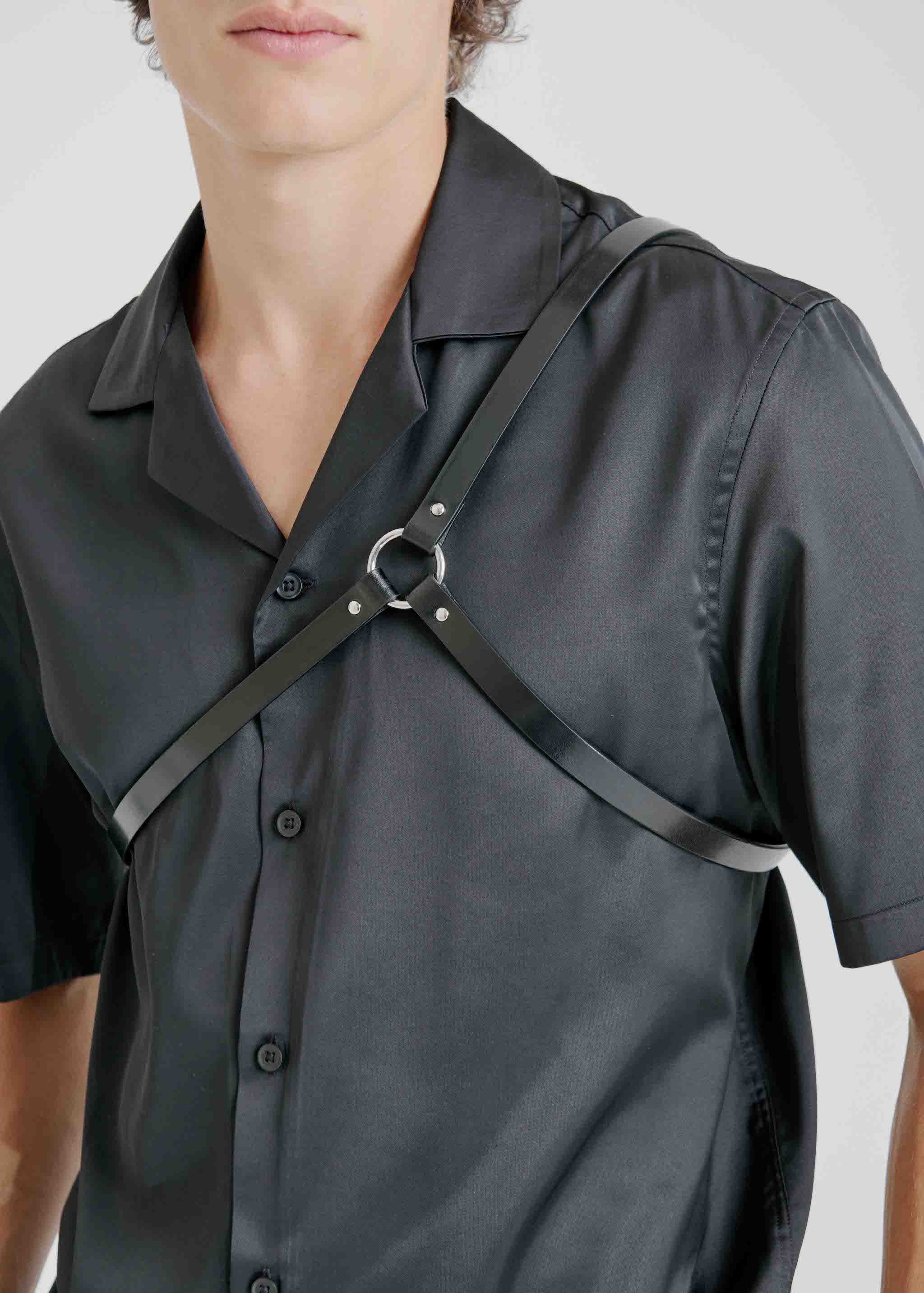 close-up of male model wearing yvy leather asymmetric shoulderpiece in black over a black short-sleeve shirt