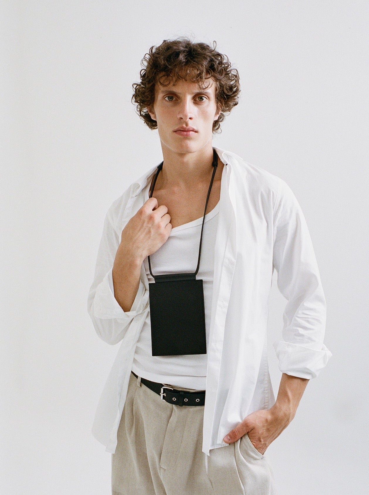 man wearing yvy leather travel wallet over neck paired with white top and beige pants