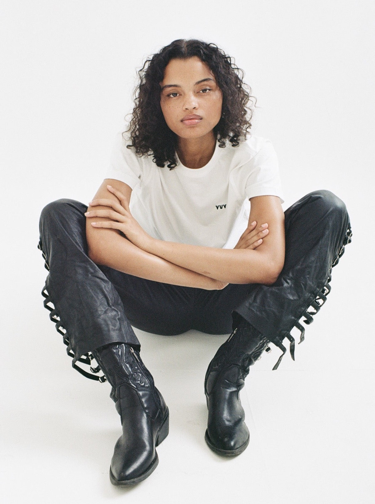 a female model wearing a classic white t-shirt with yvy logo, black buckled leather yvy pants and black cowboy shoes