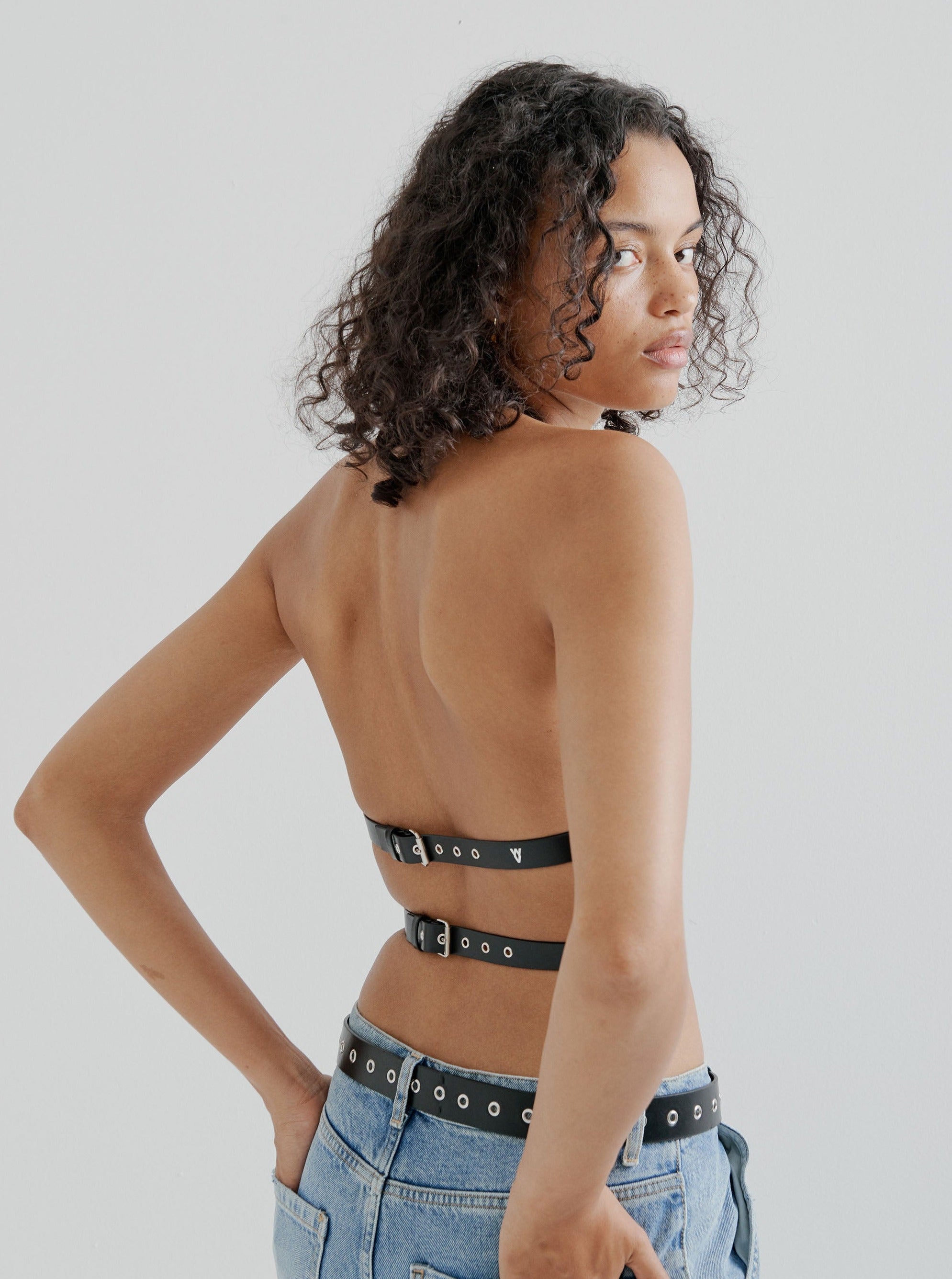 back view of model wearing black yvy leather wrap bra with denim jeans