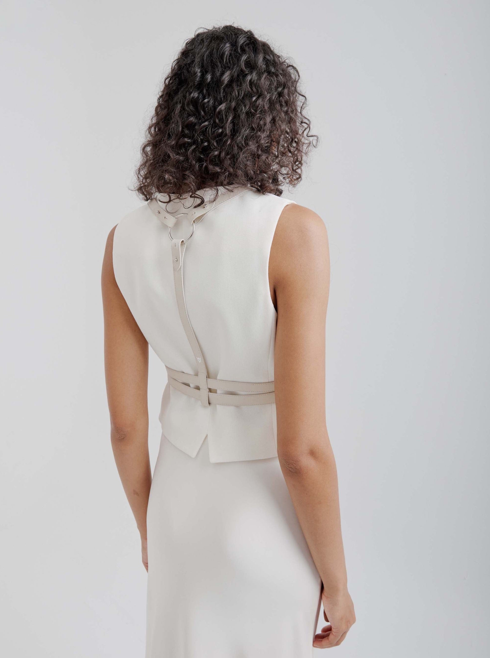 back view of female model wearing yvy leather equestrian harness in sand over white vest