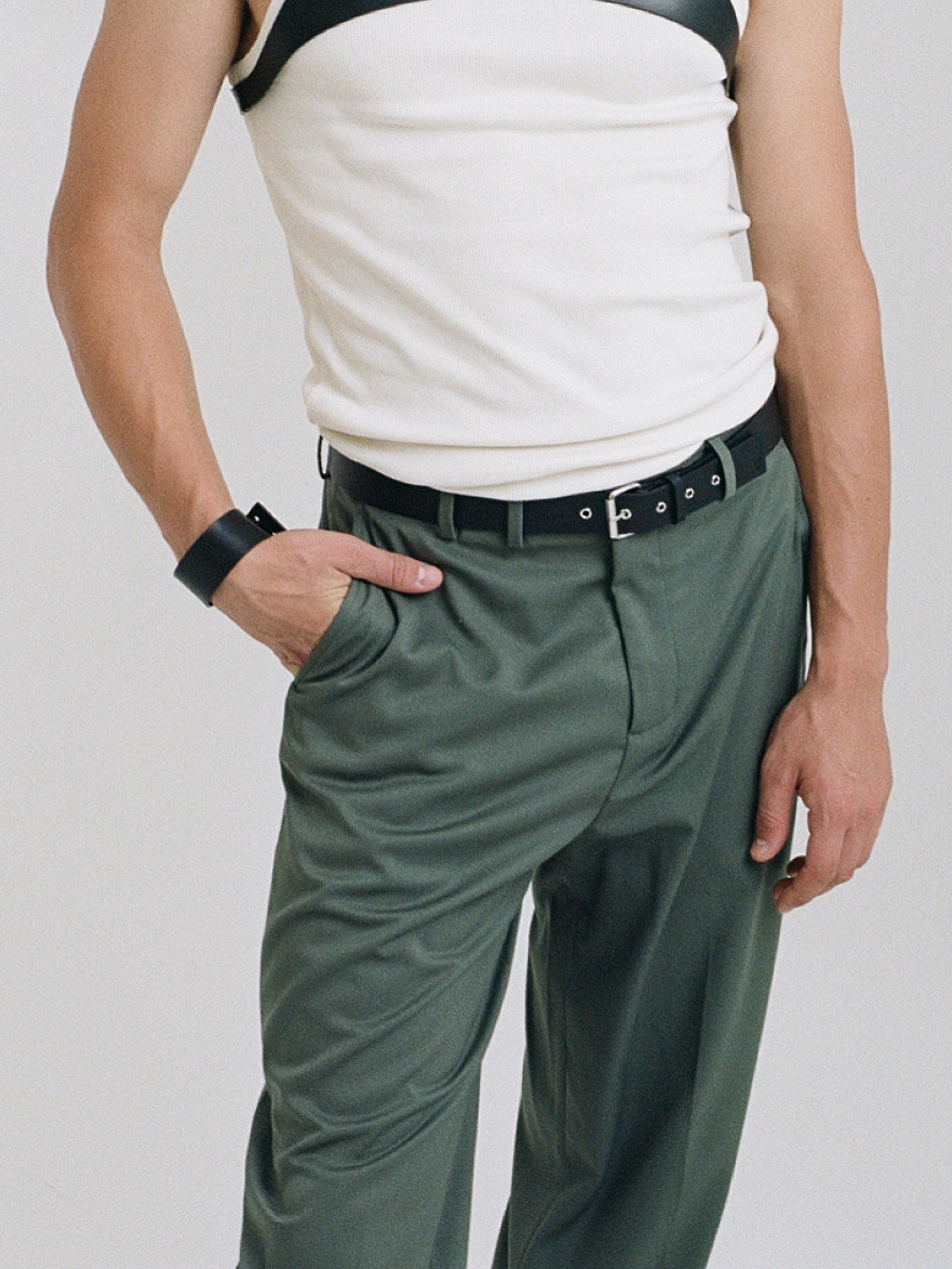 a male model wearing wide black yvy leather bracelet with silver hardware, yvy buckle belt with silver hardware, white shirt with yvy shoulder piece and olive green pants