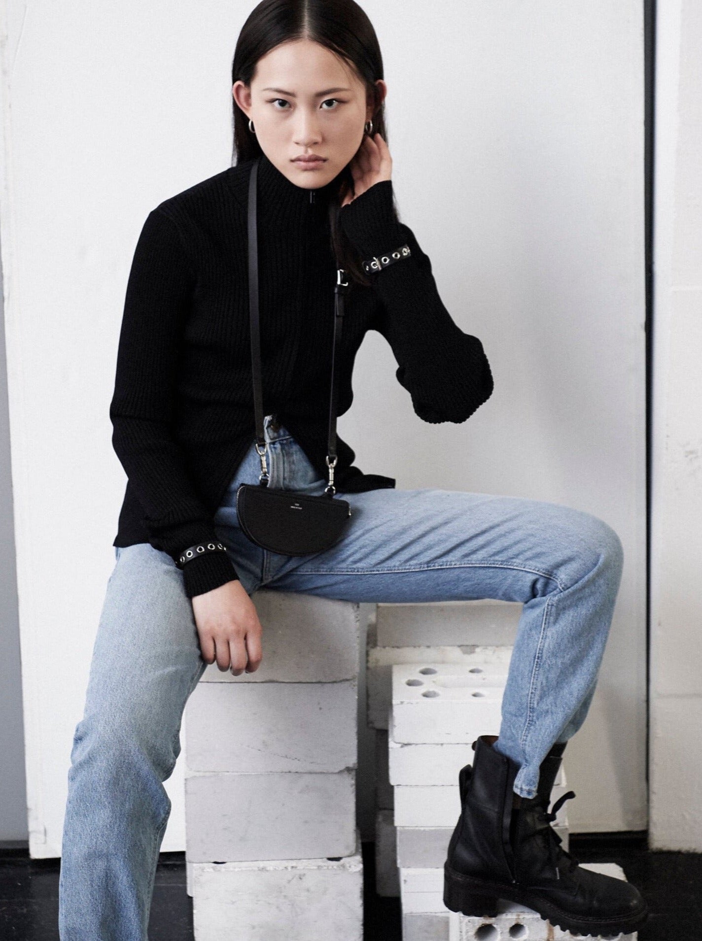 woman wearing black turtleneck and jeans with black yvy leather half moon pouch over neck with shoulderstrap