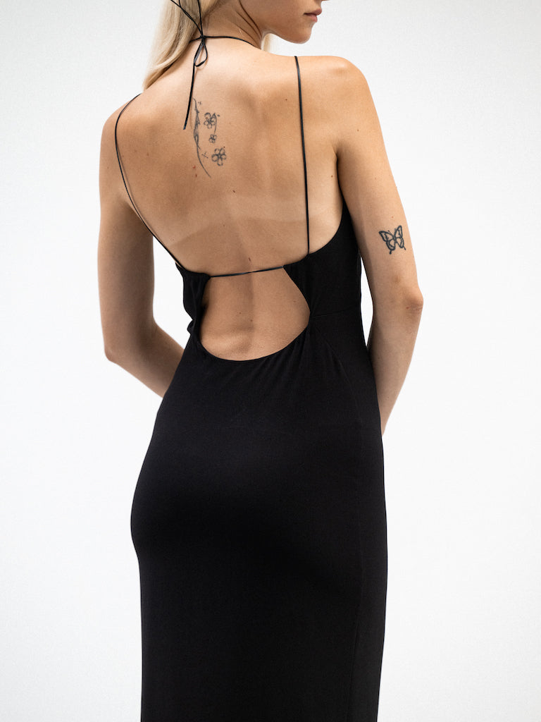 Back view of a female model wearing an elegant midi dress that features a curved open back design with plunge back, spaghetti straps, and a form-fitting silhouette