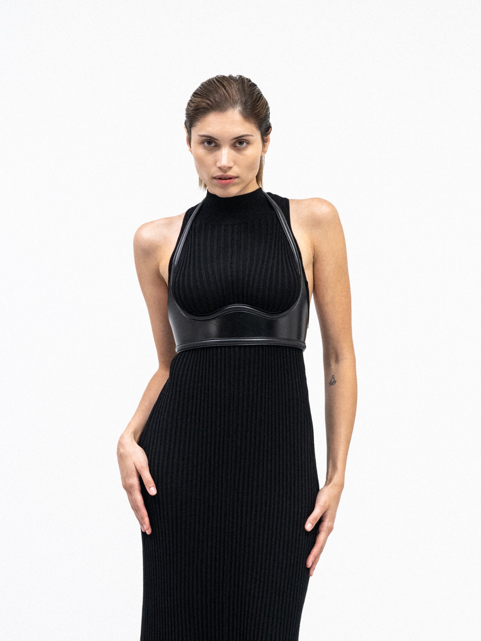 A female model in sleek yvy black ribbed knit dress with architectural yvy leather snake bustier detail 