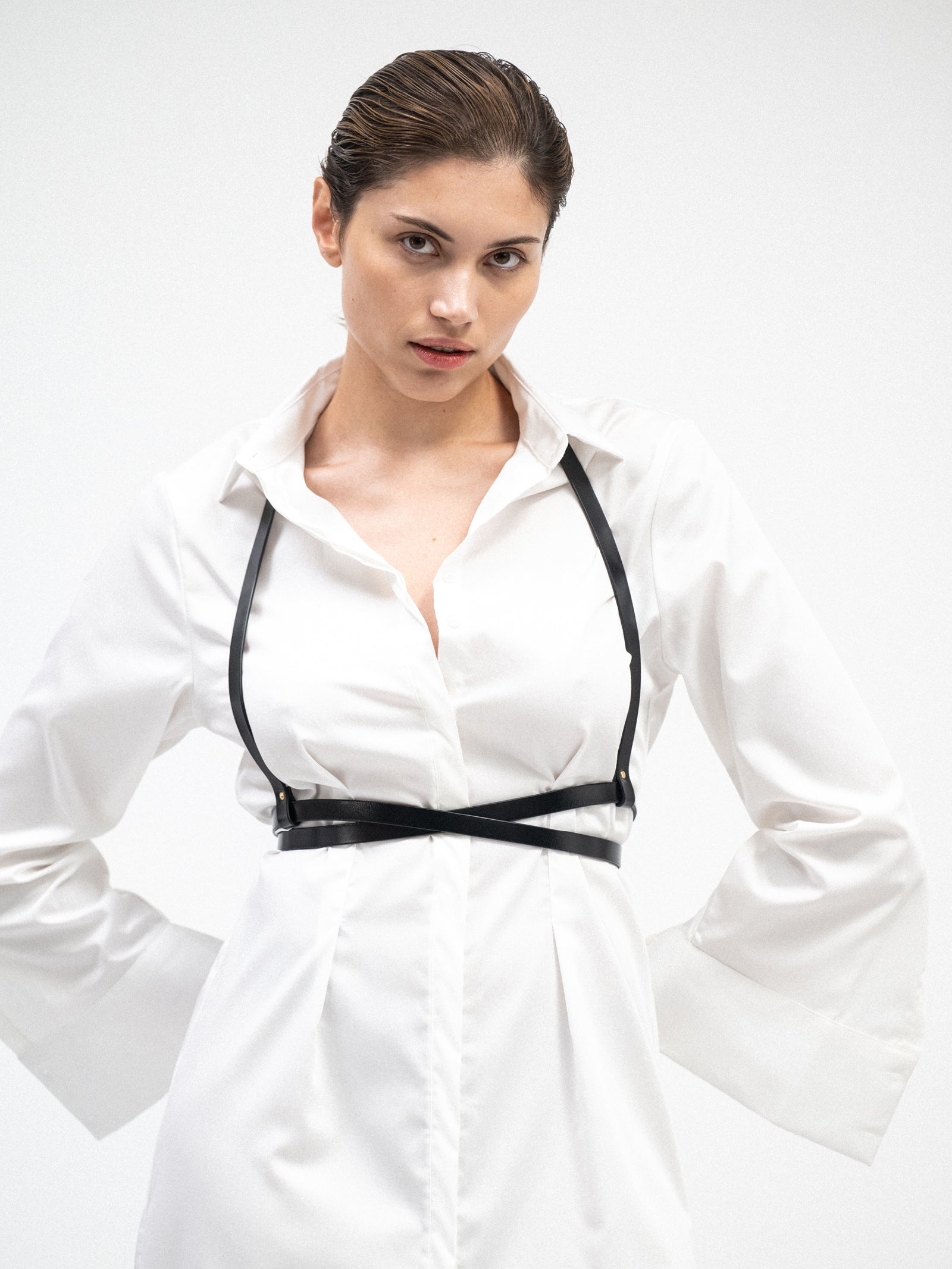 A female model wearing a white long sleeve yvy cotton shirt dress paired with a black leather harness
