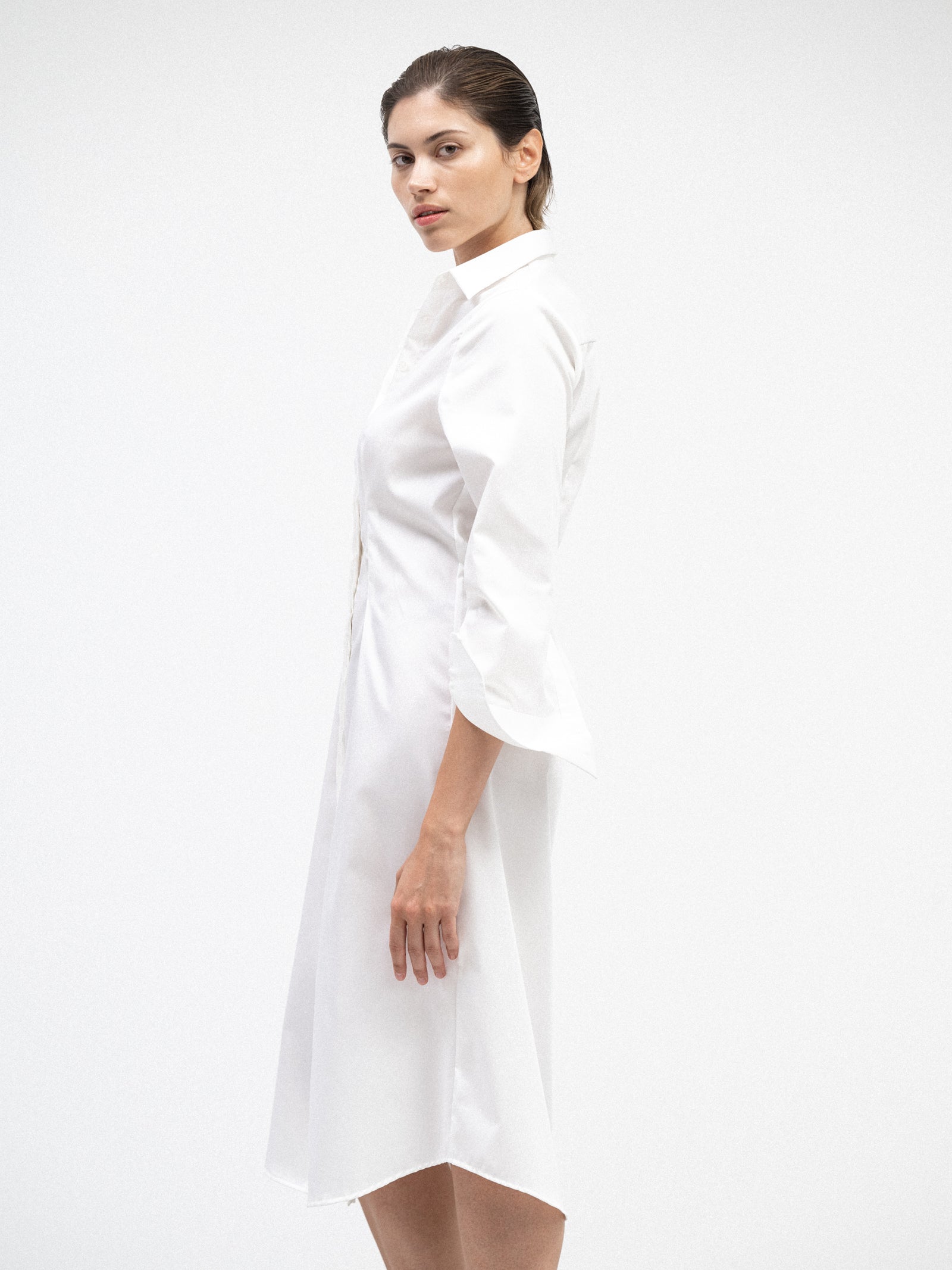 Side view of a female model wearing a knee-long white cotton yvy shirt dress