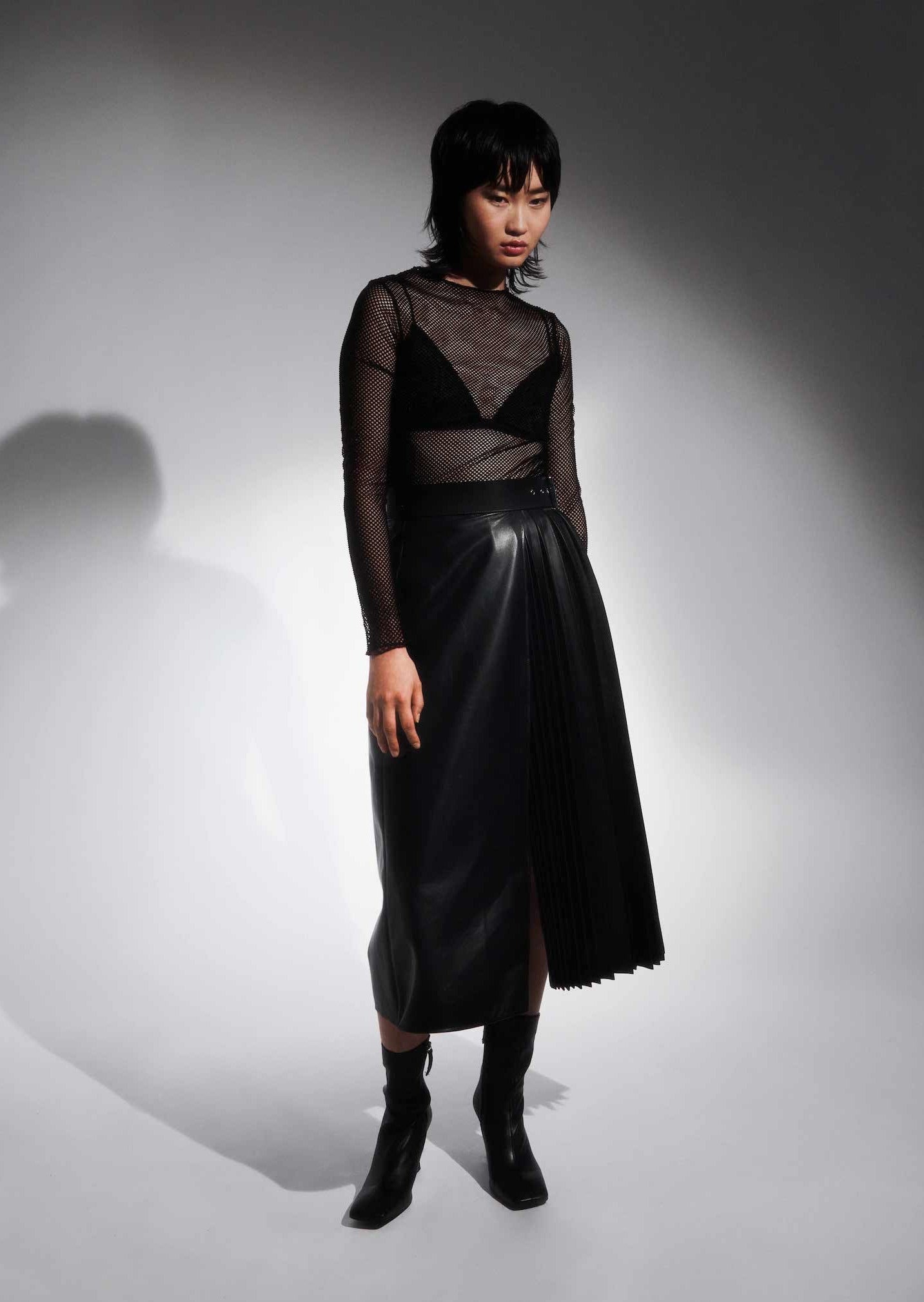 a female model wearing black midi leather yvy skirt featuring plisse leather detail and a buckle with silver hardware