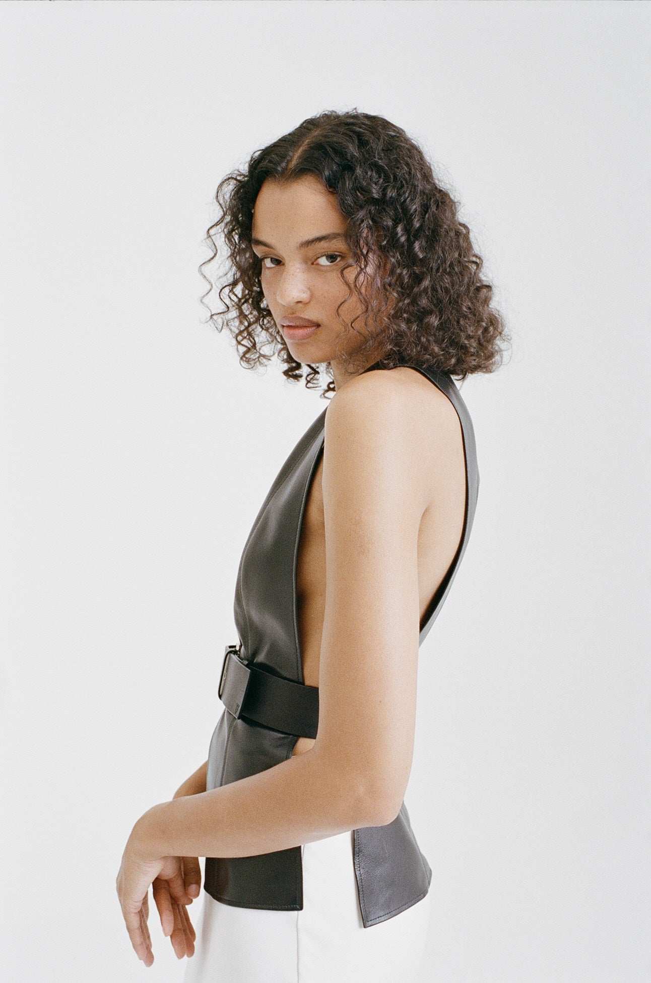 A female model wearing black belted yvy leather vest posing sideways