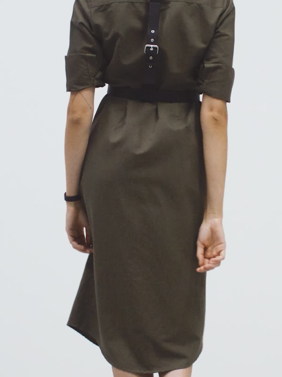 a woman posing in yvy green linen shirt dress and black harness, showcasing black ring bracelet on her wrist